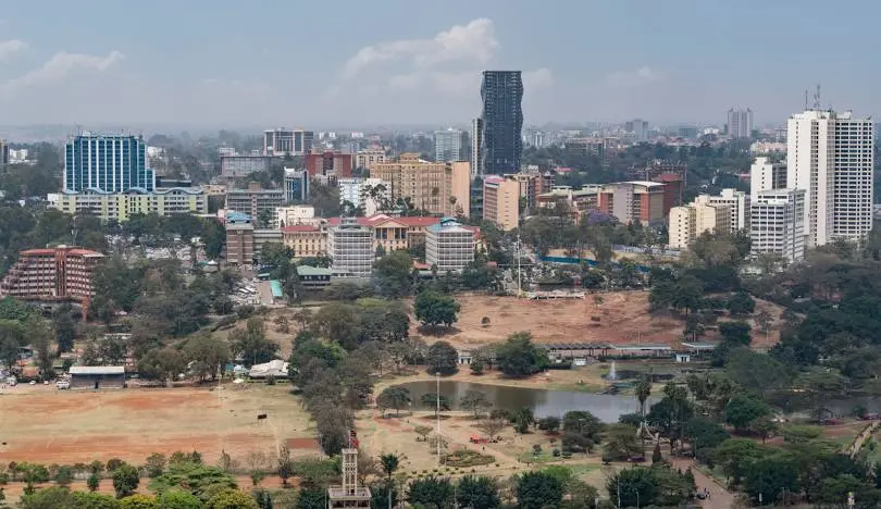 Nairobi Skyline with Wildlife: "A lion walking through the tall grass of Nairobi National Park with the city's modern skyscrapers in the background during a morning safari.