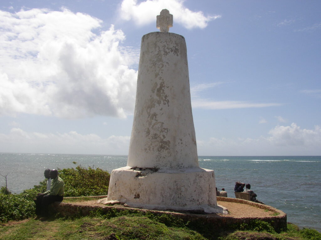 The weathered limestone Vasco da Gama Pillar, showing the protective concrete cone added for reinforcement, situated on a flat rocky cliff.